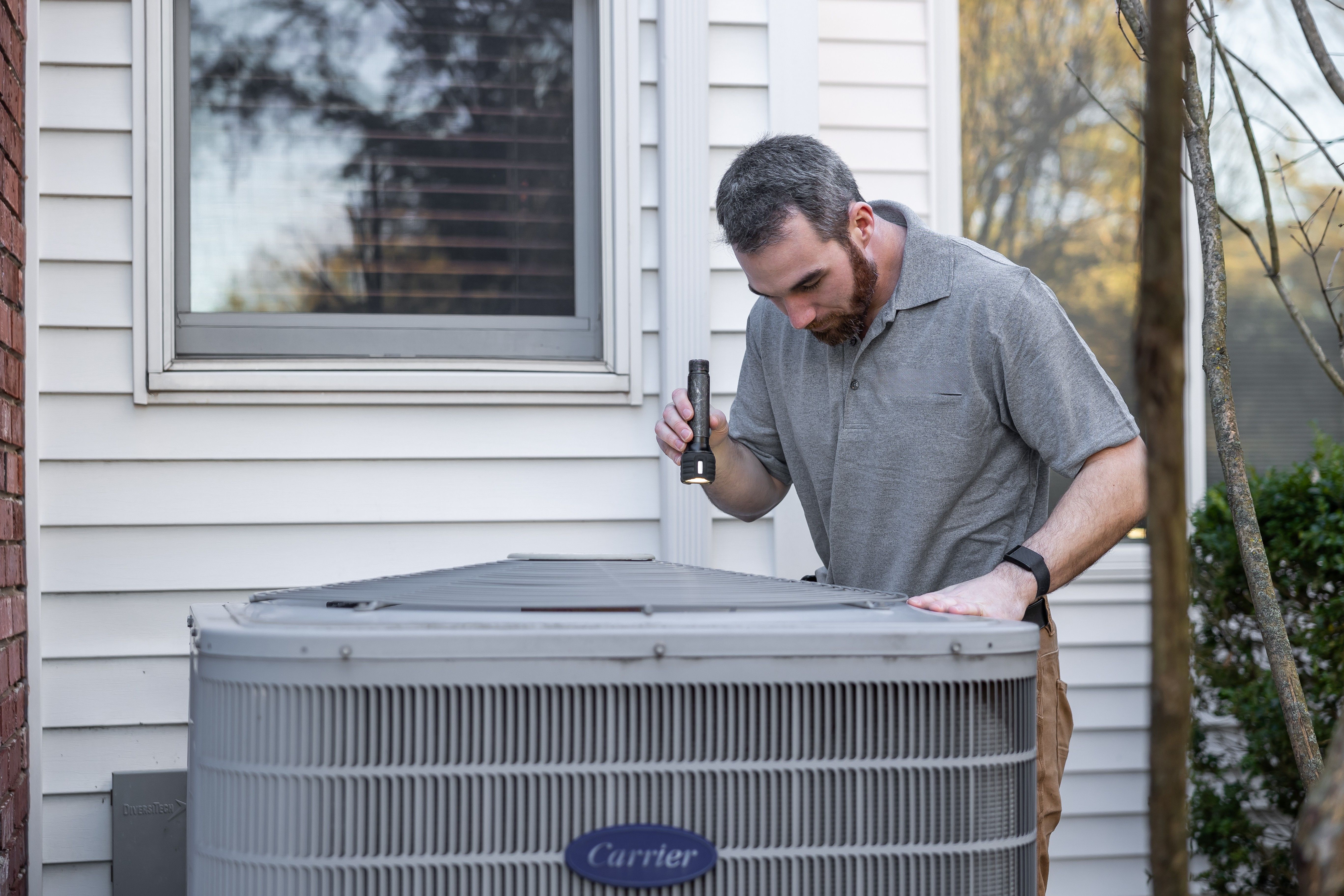 Technician inspecting an outdoor HVAC unit on a home service call